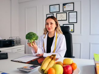 Female nutritionist in office holding broccoli, surrounded by fruits, promoting healthy lifestyle.